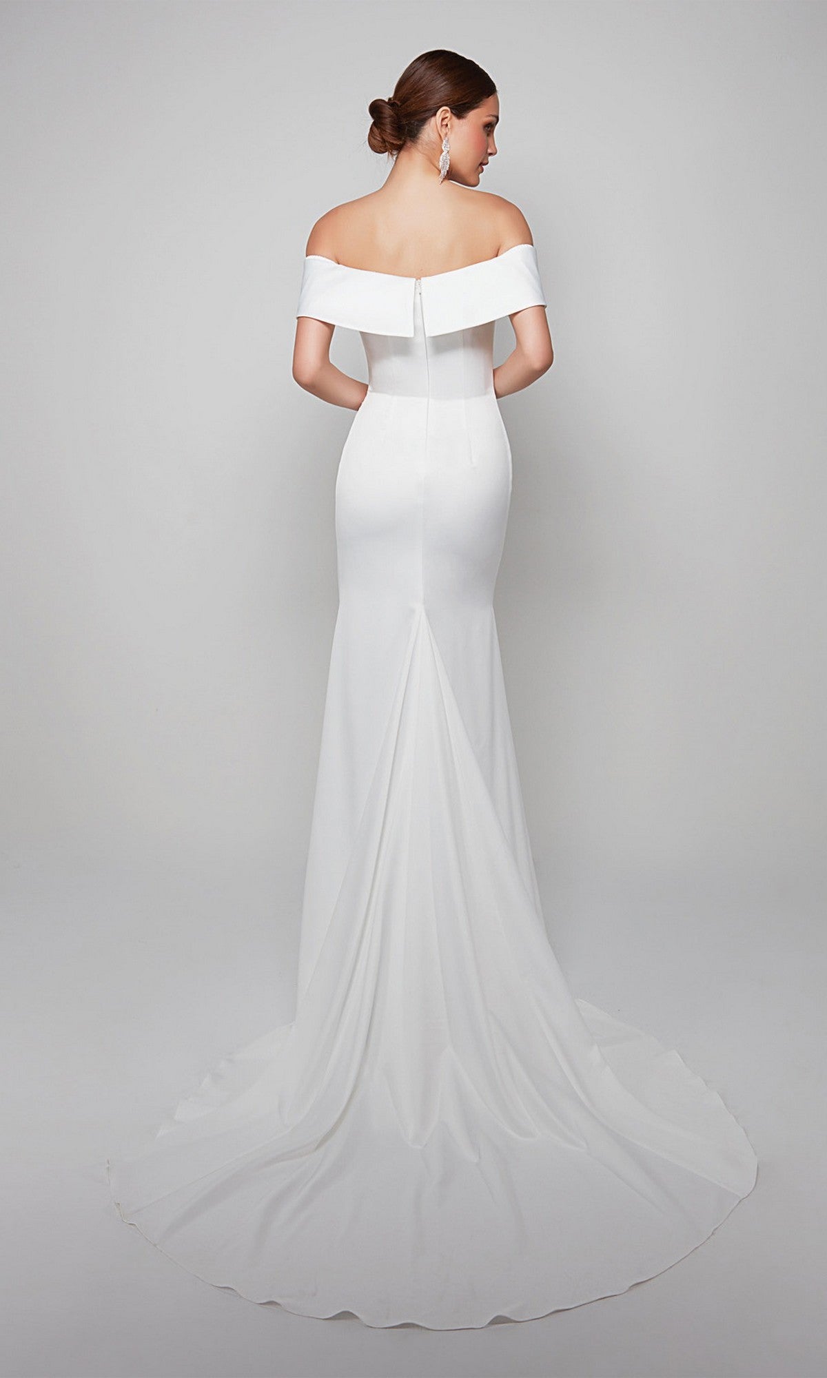 A woman in the Long White Dress: Alyce 7059—an off-shoulder, fitted gown with a flowing long train—stands facing away against a plain light background.